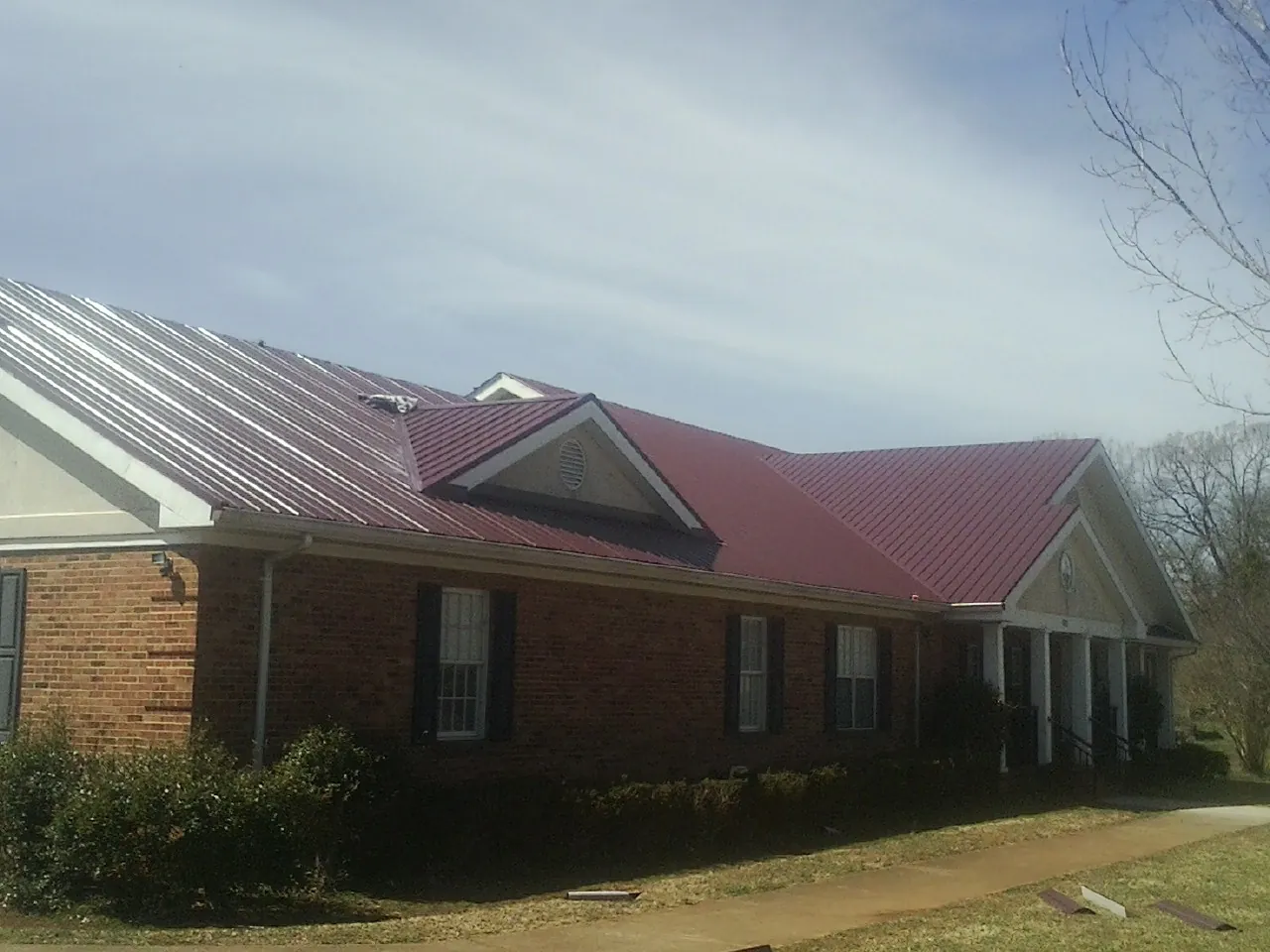 Red metal roof with gabled entries on a long brick building, from a Hail Damage Roof Repair job in Satsuma