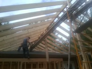 Rafters going up over a new addition with a worker on the wall in Satsuma