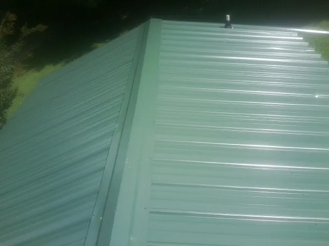 New green metal panels meeting at the ridge of a roof — Flat Roof Repair work by our crew in Satsuma