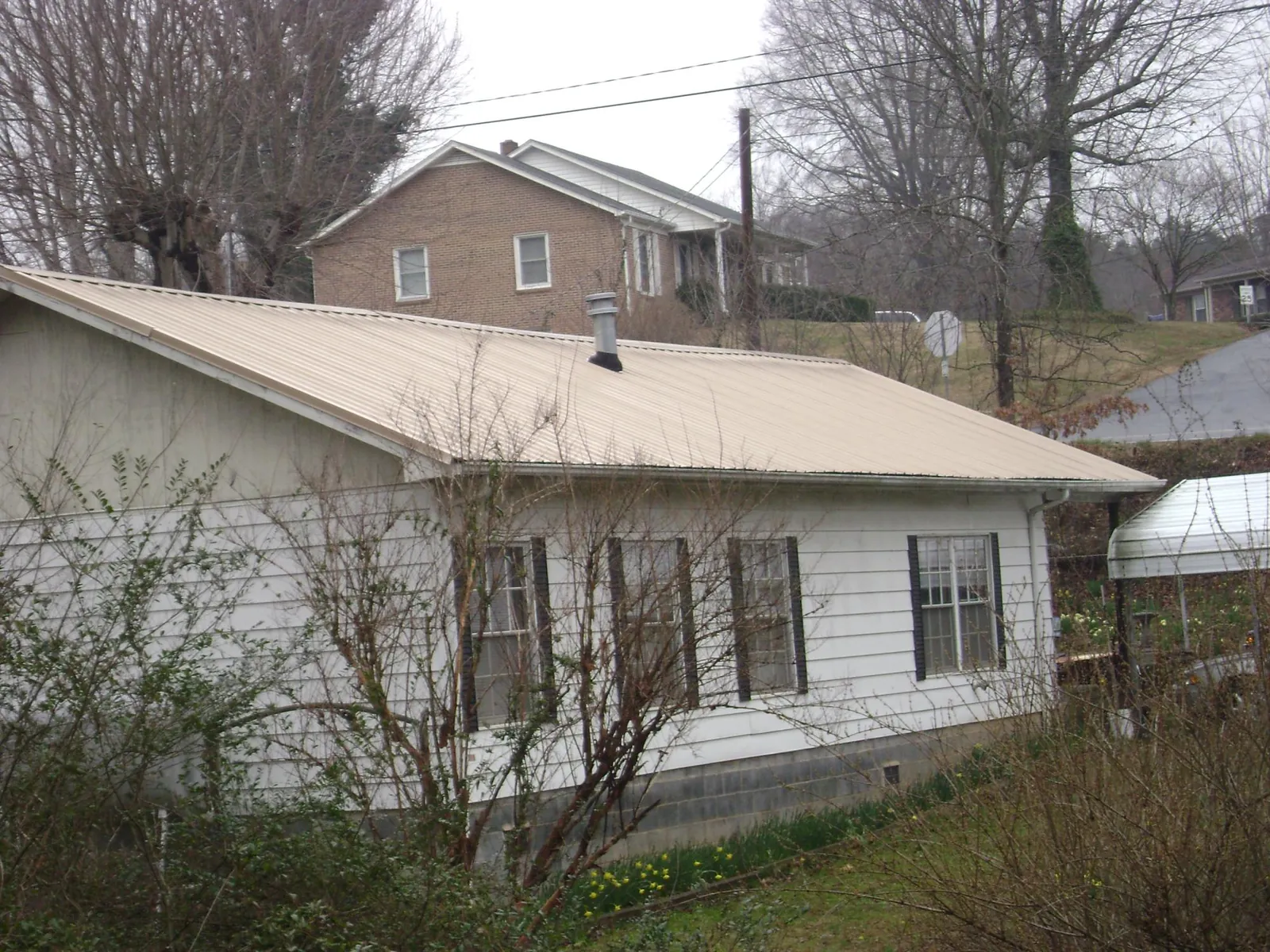 Tan metal roof on a white sided house set into a hillside — Commercial Roofing by Roofing Brothers in Satsuma